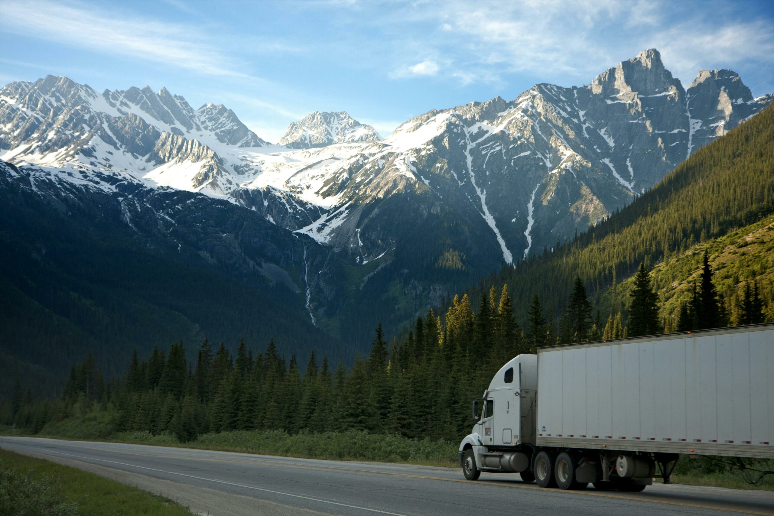 Scenic View Of A Truck Traveling Near Snowy Mountains